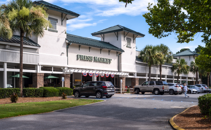 Fresh Market with cars in front lot and palm trees on the sides.