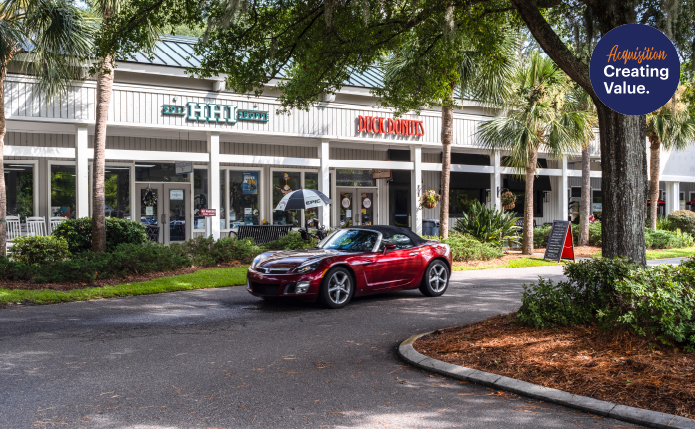 Red sports car drives past Duck Donuts storefront and palm trees.