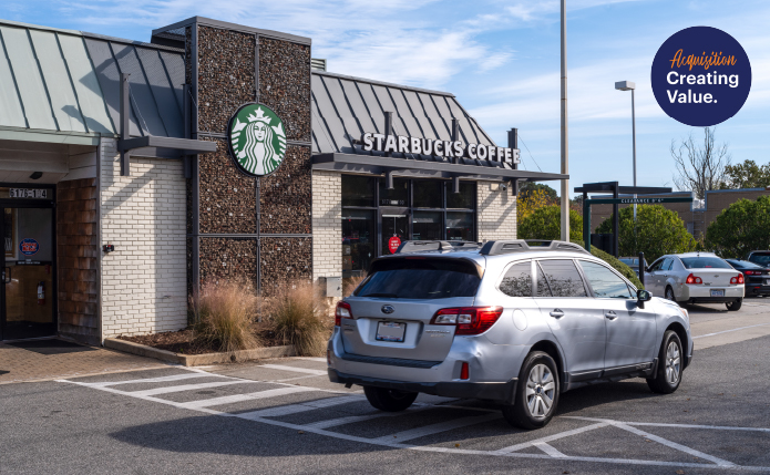 Grey SUV passing Starbucks into tree-lined lot.