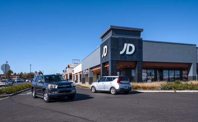 Truck and SUV pass in front of JD Sports store.