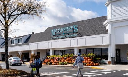 McCaffrey’s Food Market at Village at Newtown in Newtown, PA, shown with classic white clapboard architecture, teal signage, large covered walkway, and seasonal outdoor produce displays including pumpkins arranged along the storefront.