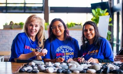 Three women in Brixmor Service Day Shirts writing messages of kindness on stones