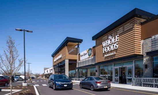 Cars pass Whole Foods Market on access road at shopping center.