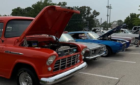 a line of cars at a car show with hoods popped