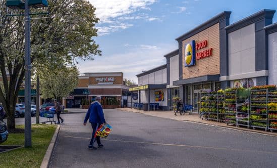 Shopper under a tree approaching Lidl grocery store in Long Island.