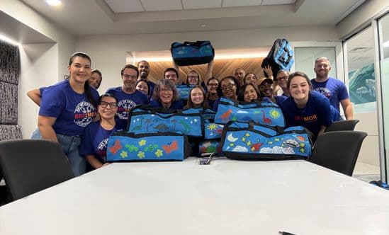 group of people in blue shirts pose around large blue duffle bags