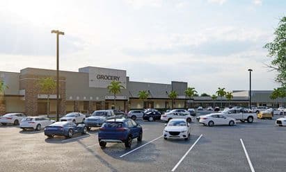 Updated grocery‑anchored retail building at Sunrise Town Center in Sunrise, FL, shown with stone accent columns, wide sidewalks, palm‑lined frontage, and customer vehicles filling the surrounding parking area.