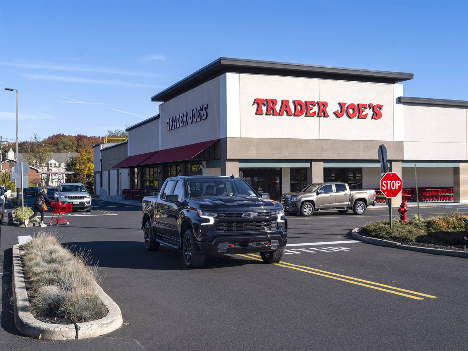 Trader Joes entrance with Black truck and customer walking with shopping cart