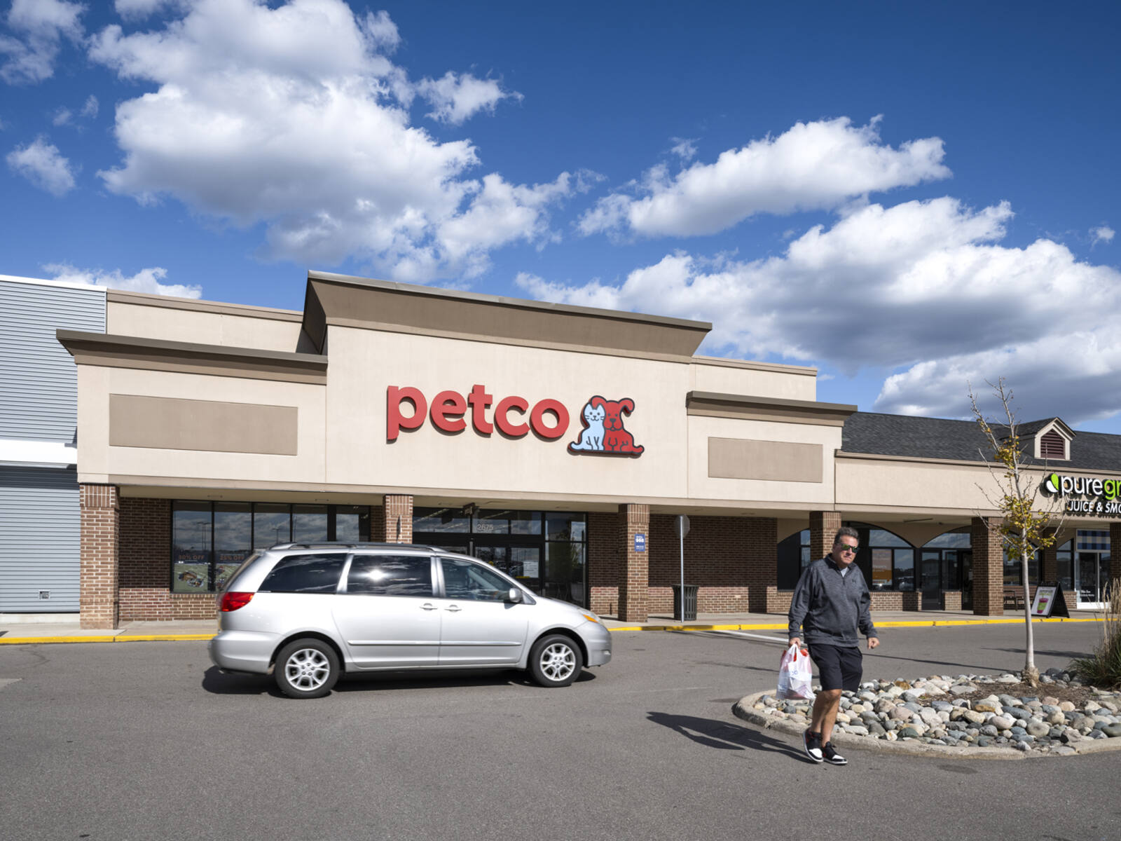 Man leaving Petco into parking lot with grey minivan behind him.