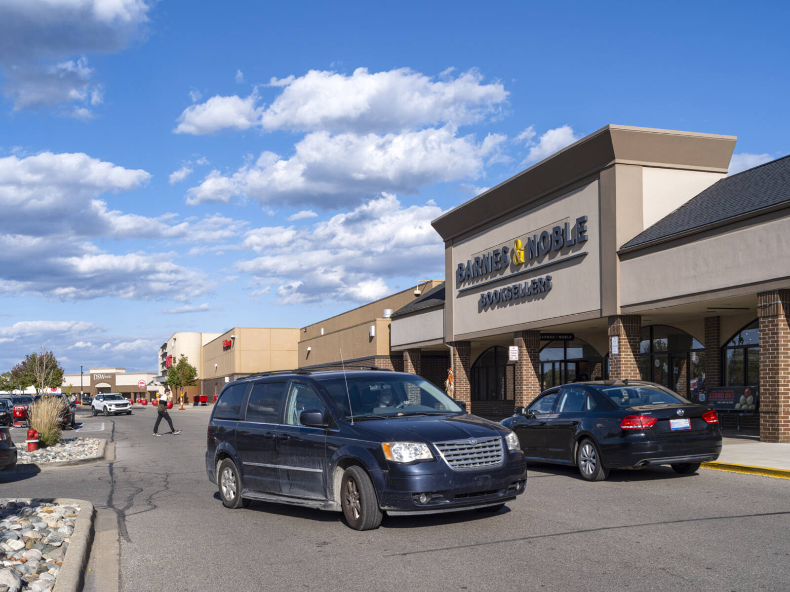 Two dark cars turning in front of Barnes & Noble store in a parking lot.