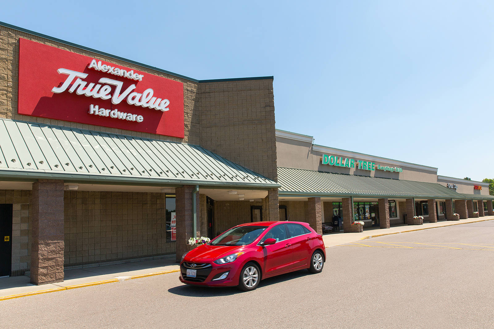 Red SUV driving past True Value hardware store in Farmington, MI.