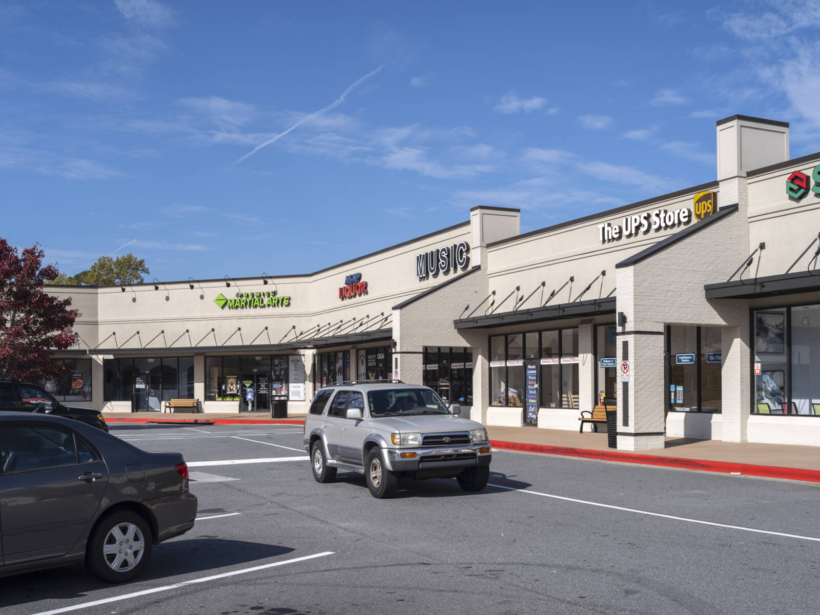 Grey SUV passes UPS store on access road.  