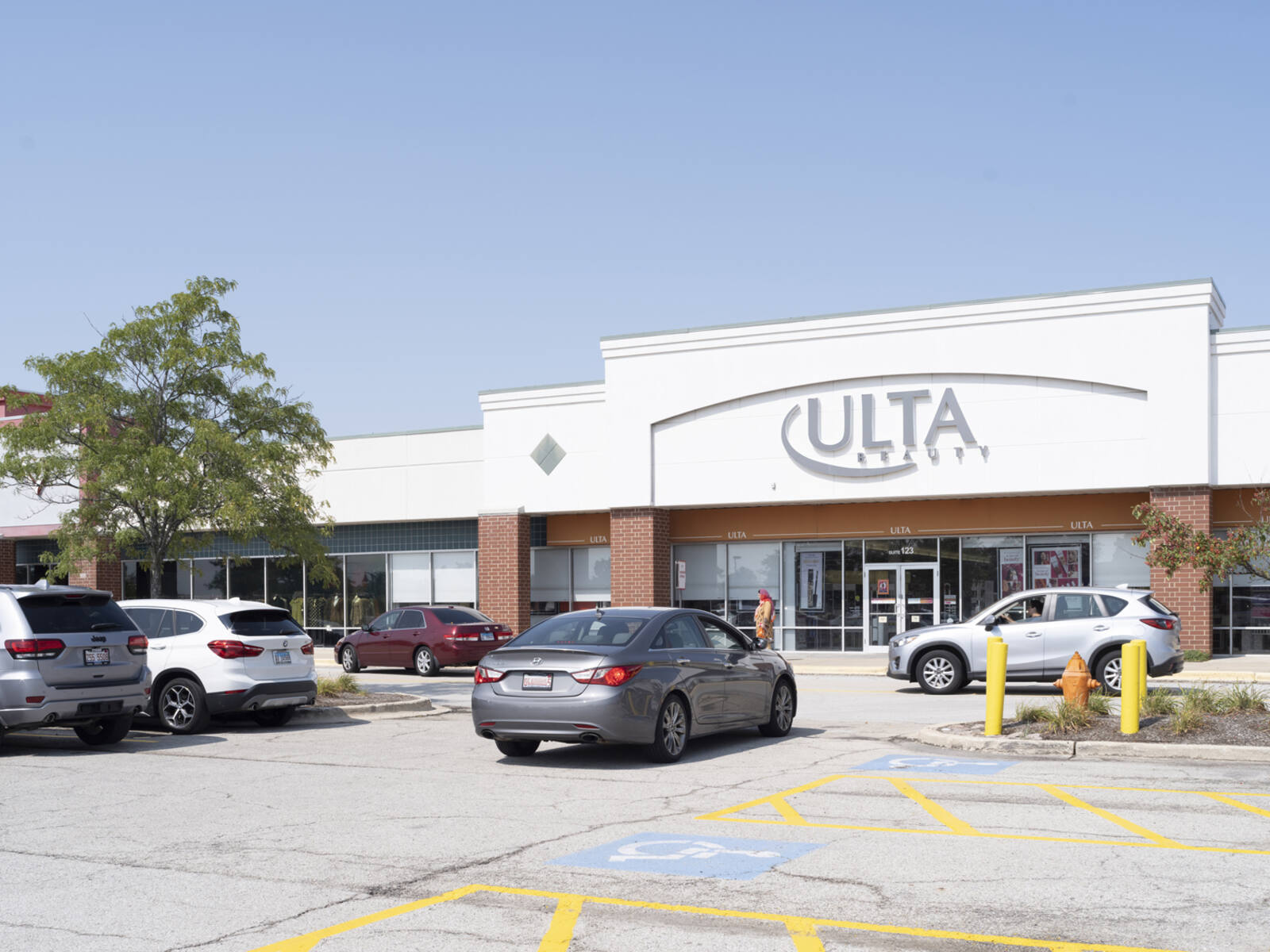 Busy parking lot in front Ulta Beauty with large tree on left.
