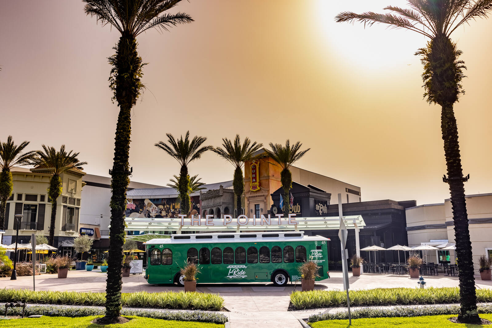 Green bus and palm trees over Pointe Orlando sign on a sunny day.