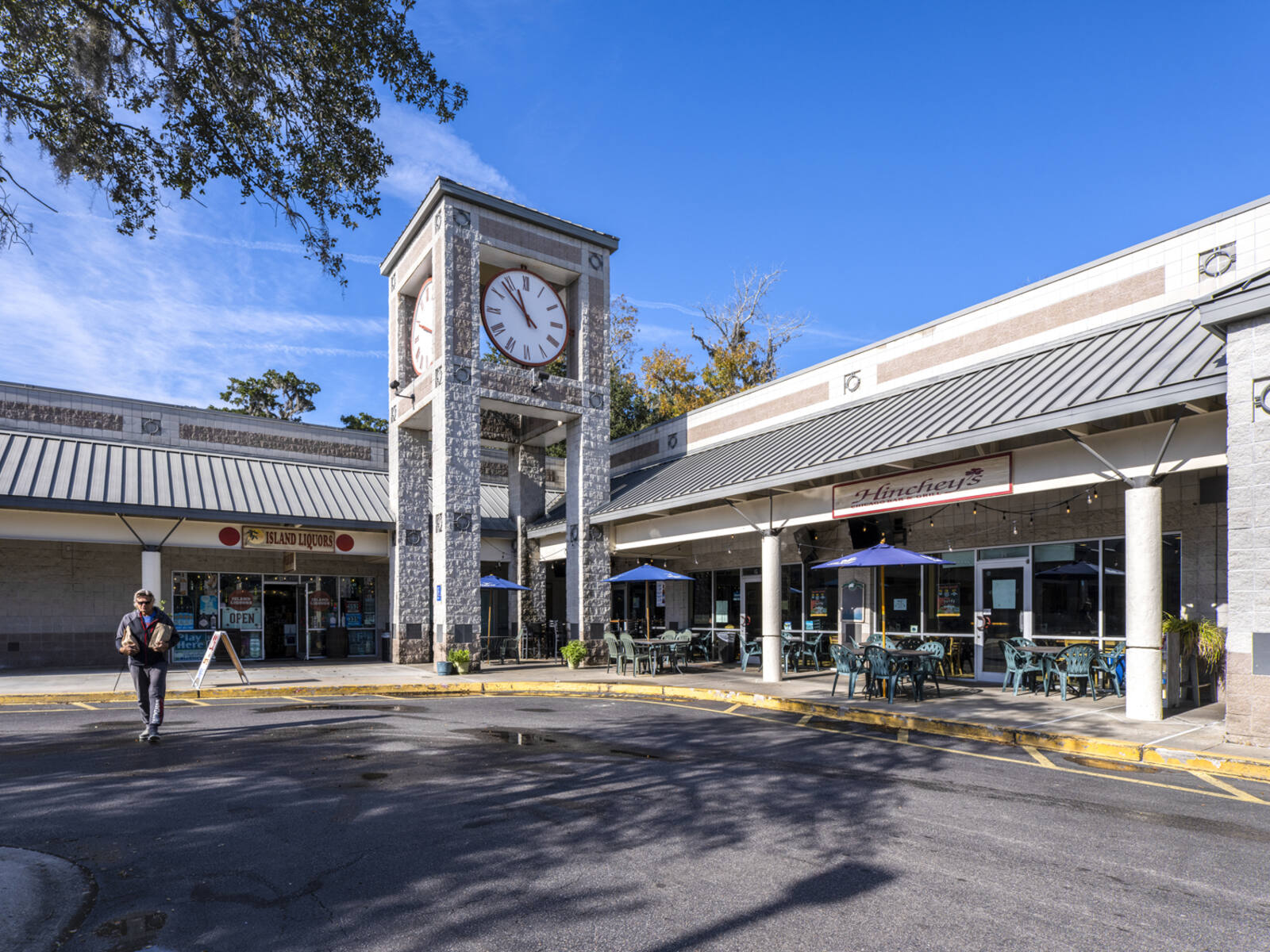 Man with bags exiting shopping center with clock tower behind him.
