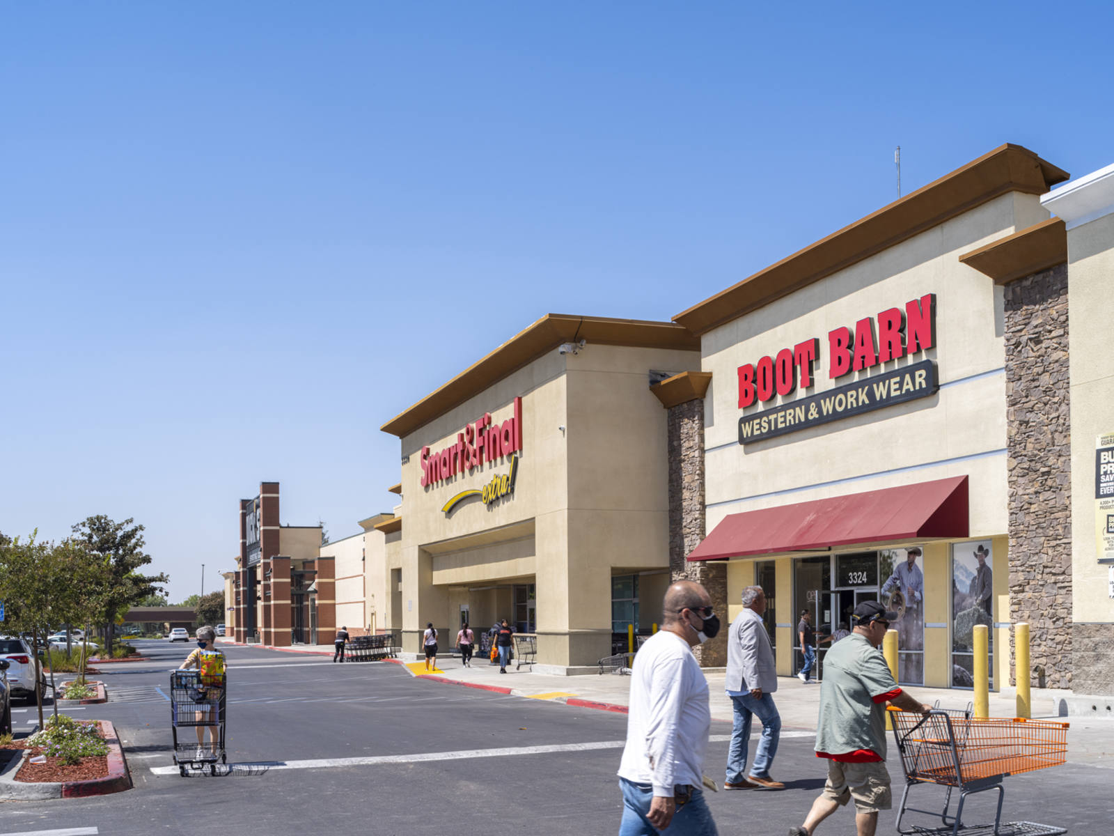 Shoppers pushing carts enter retail center with Boot Barn and Smart and Finals stores.