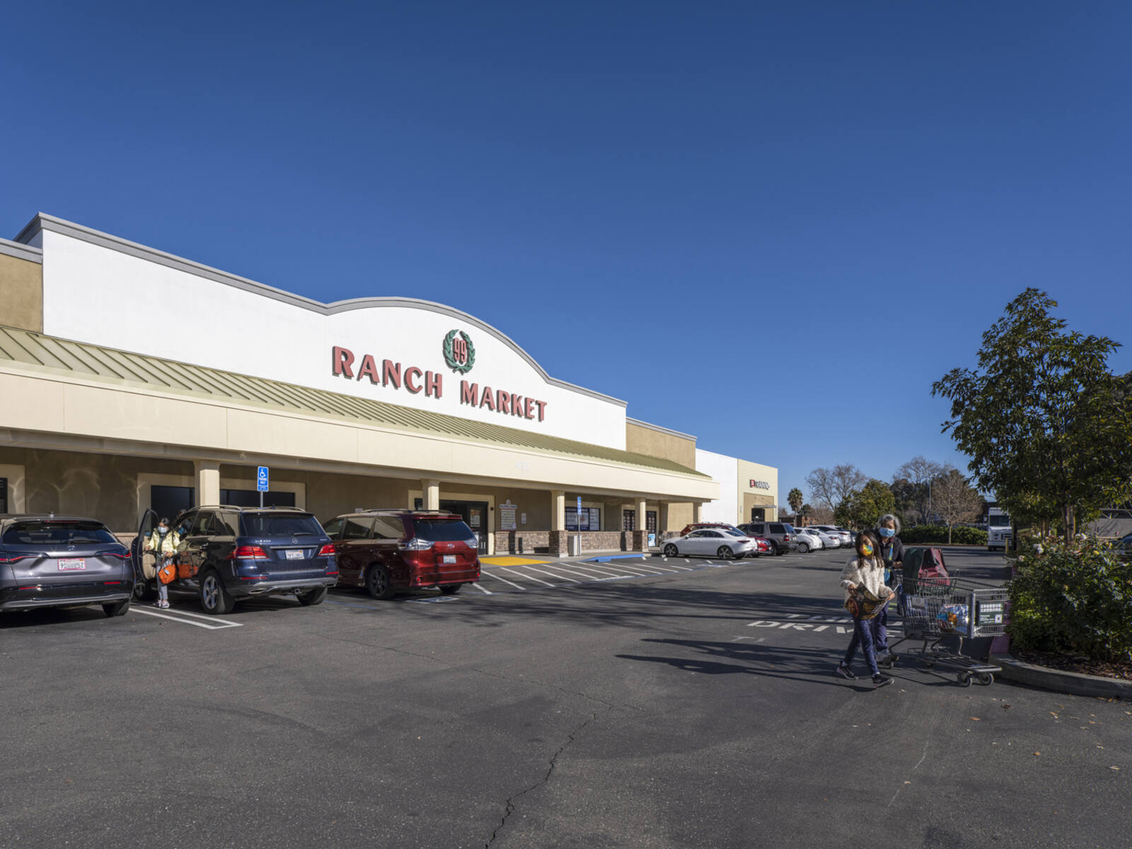 Women with cart exiting lot at Ranch Market grocery store.