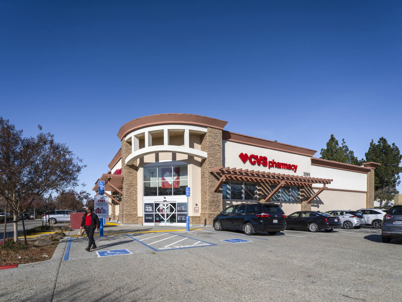 Man exiting CVS Pharmacy with busy parking lot.