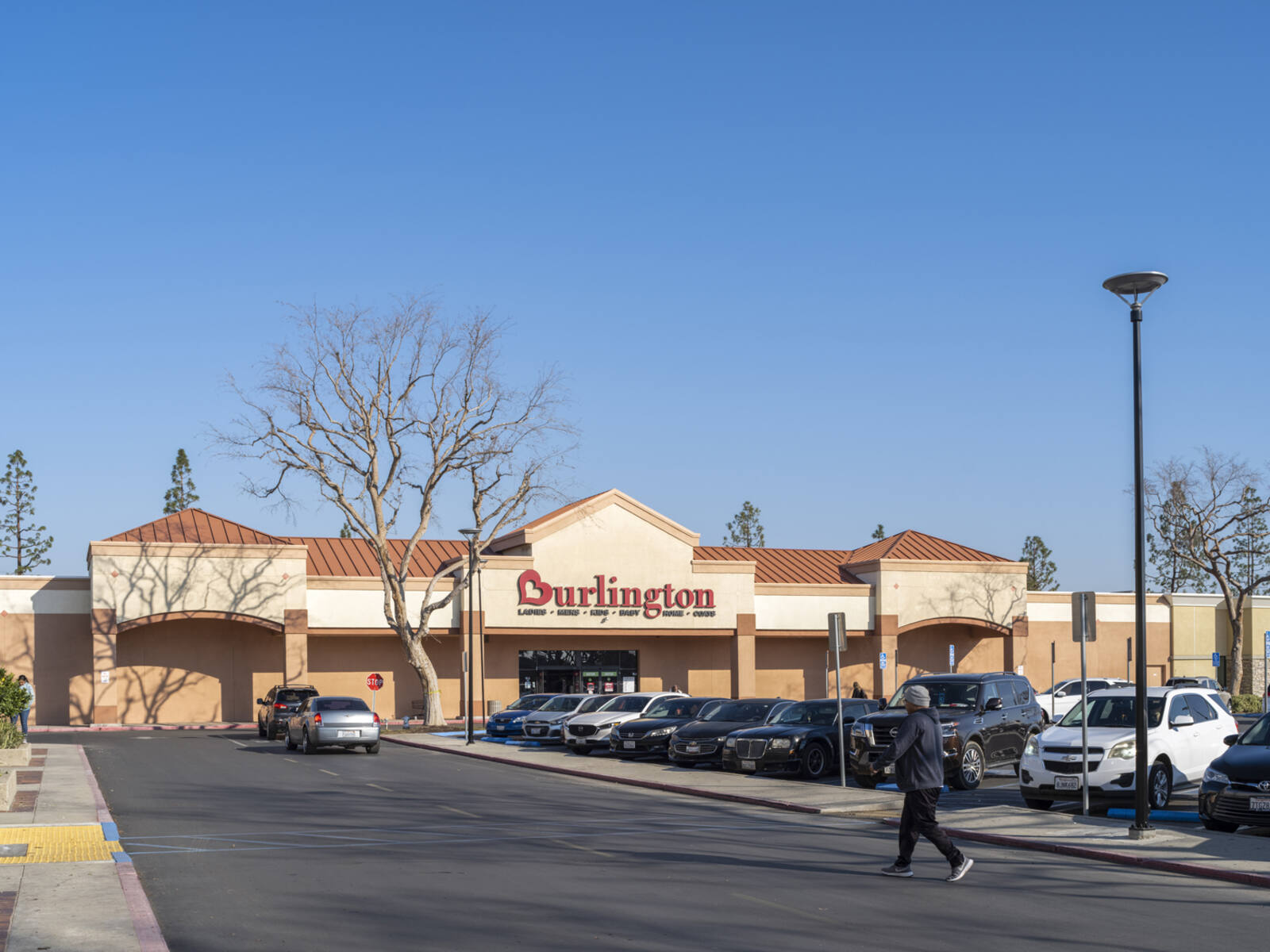 Busy parking lot and pedestrian on road walking towards Burlington store.