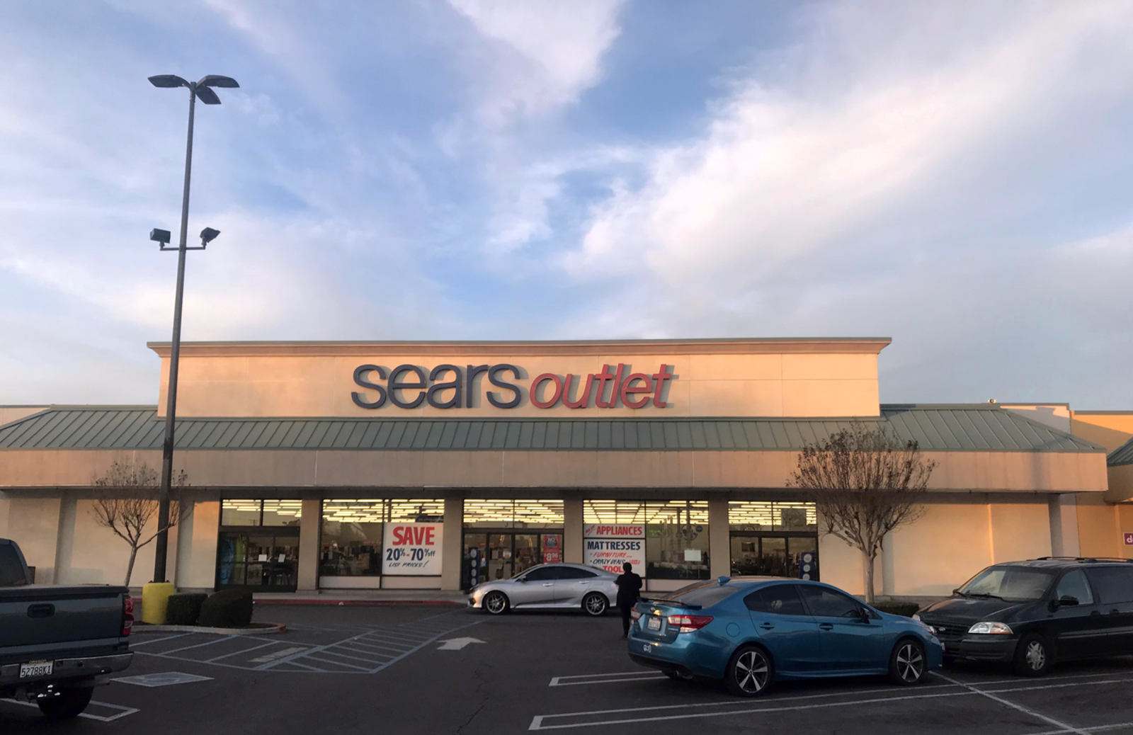 Cars and small trees in the parking lot of Sears Outlet.