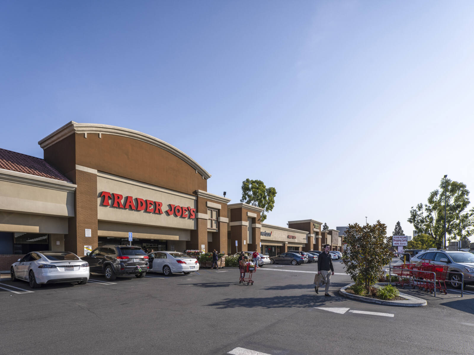 Customers with bags and carriages crossing road into parking lot at Trader Joe's.