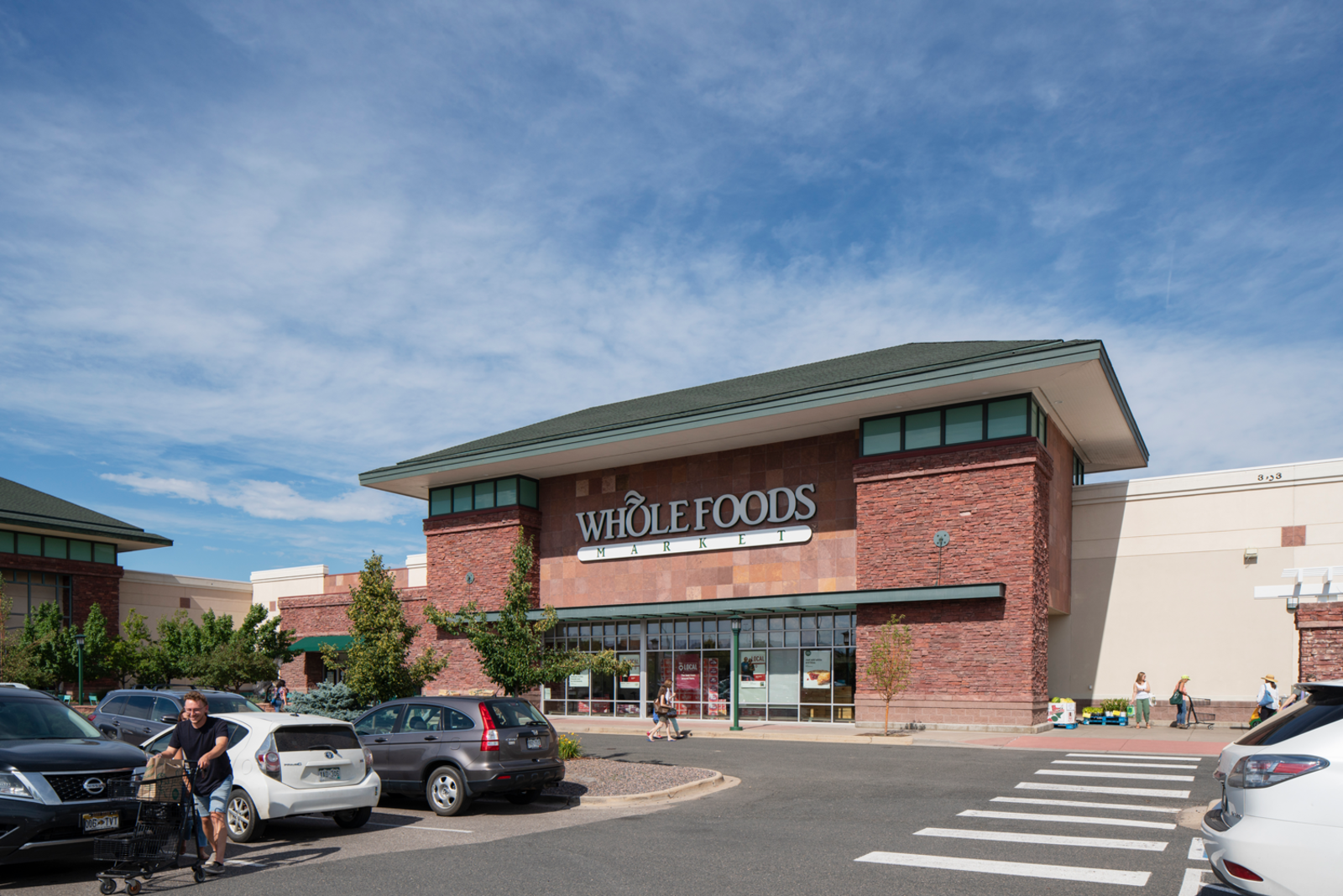 Person pushing shopping cart through full parking lot of Whole Foods