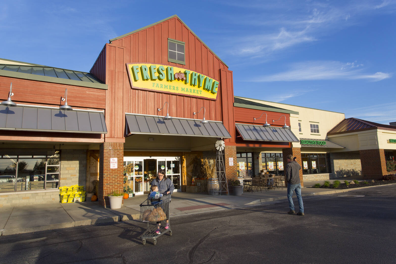 Mother with child and shopping cart exiting Fresh Thyme supermarket at Harpers Station.