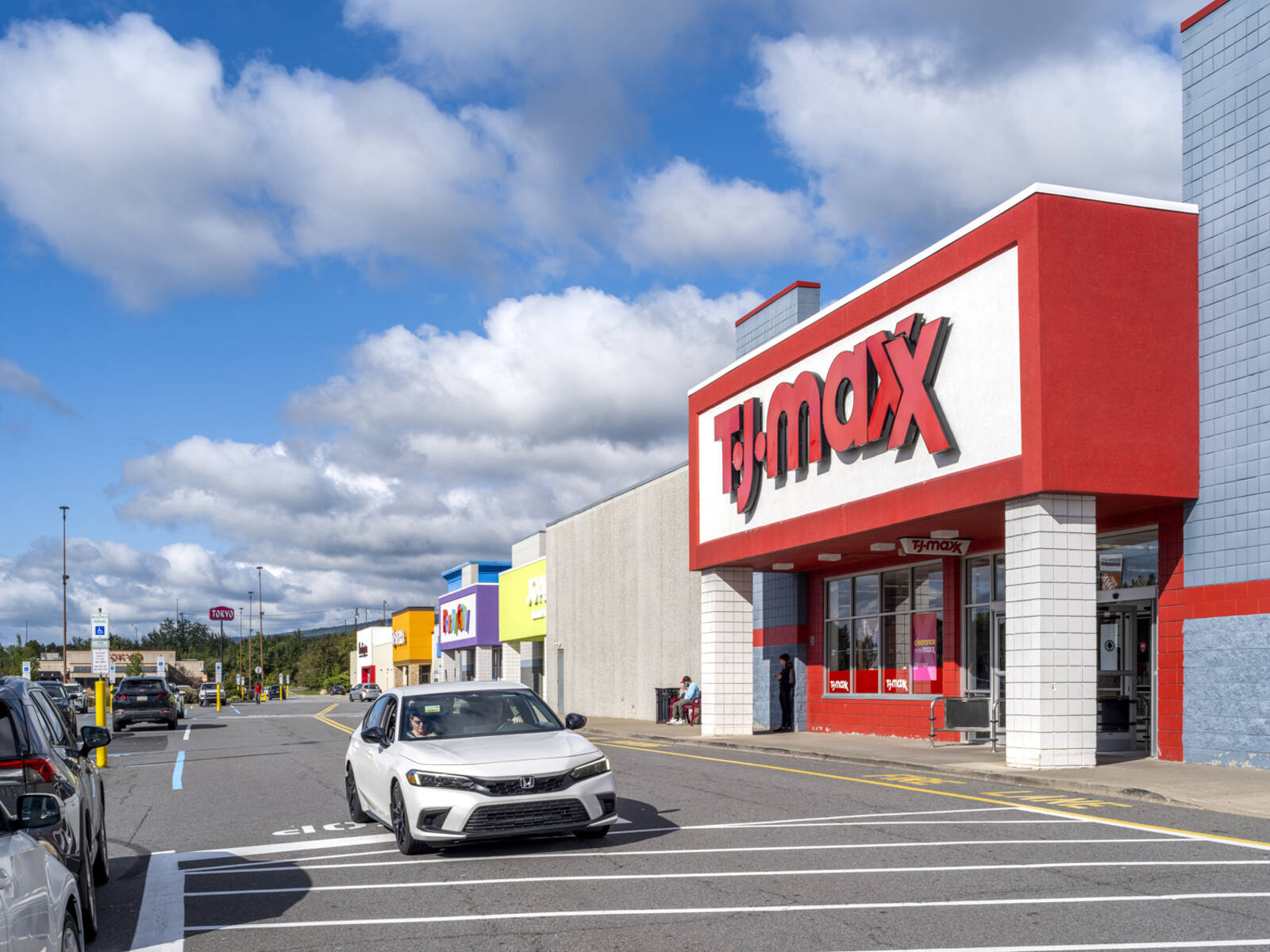 White car passing TJ Maxx on access road.
