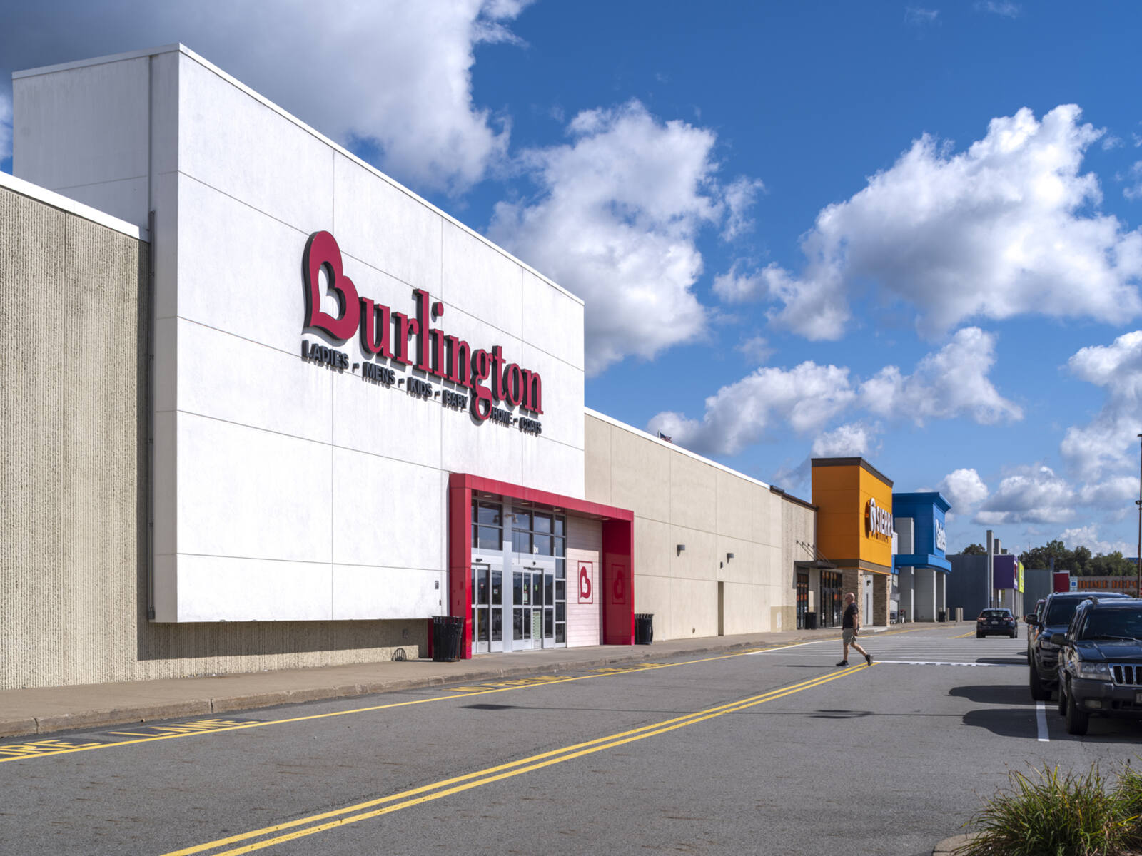 Man crossing street to enter Burlington store in shopping center.