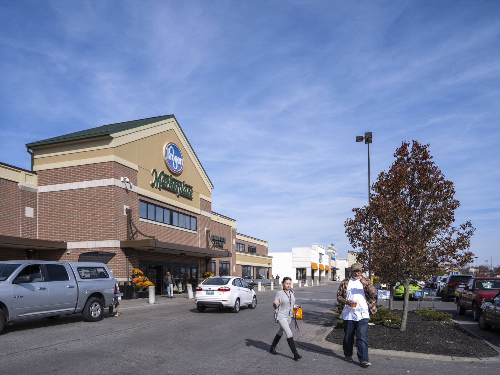 Pedestrians in front of Kroger Marketplace with cars pulled up and unloading.