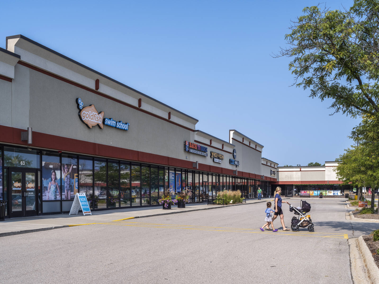 Woman with child and stroller exiting Goldfish Swim School to parking lot area.