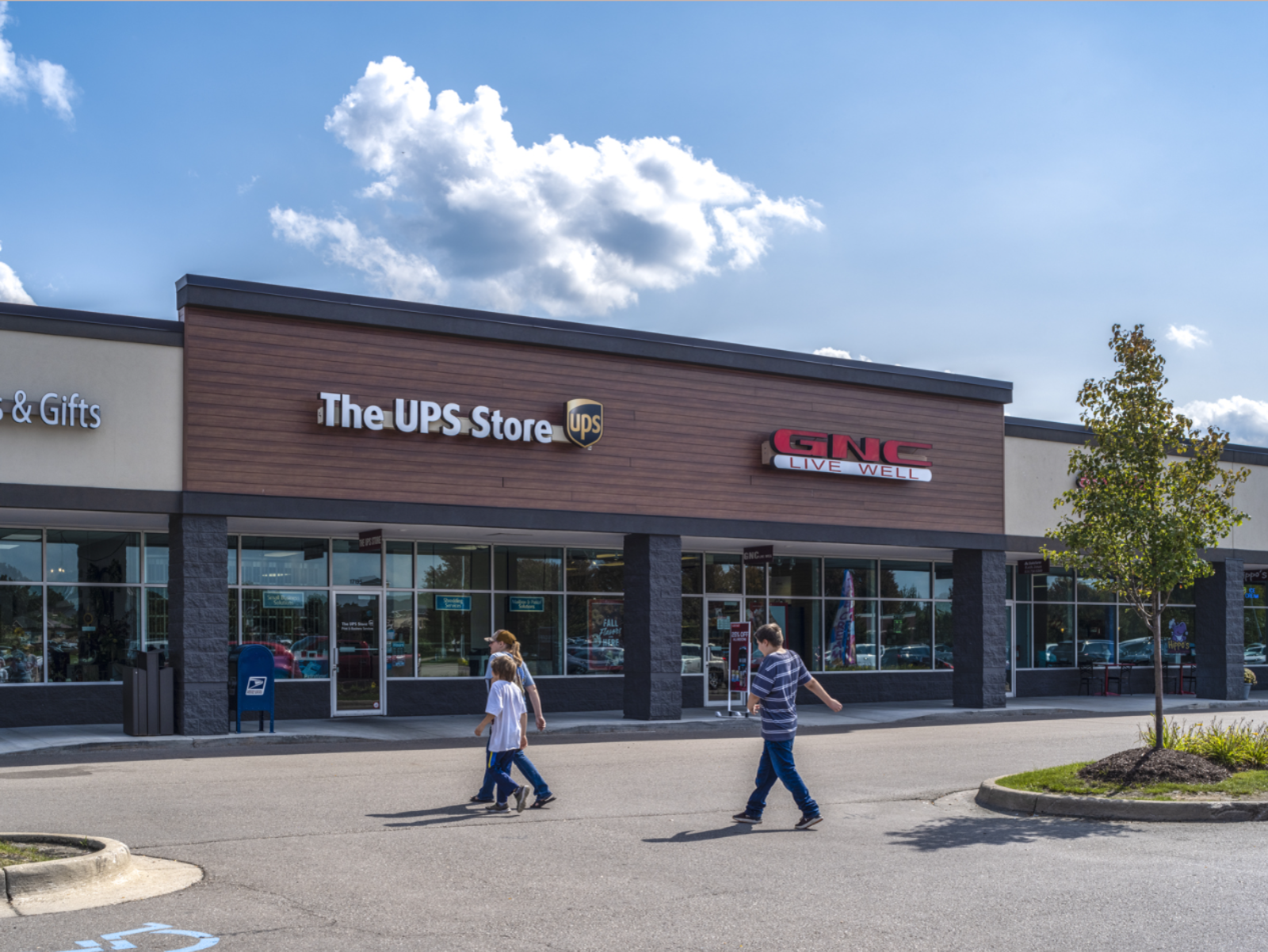Woman and 2 children in crosswalk by the UPS Store and GNC Live Well store.