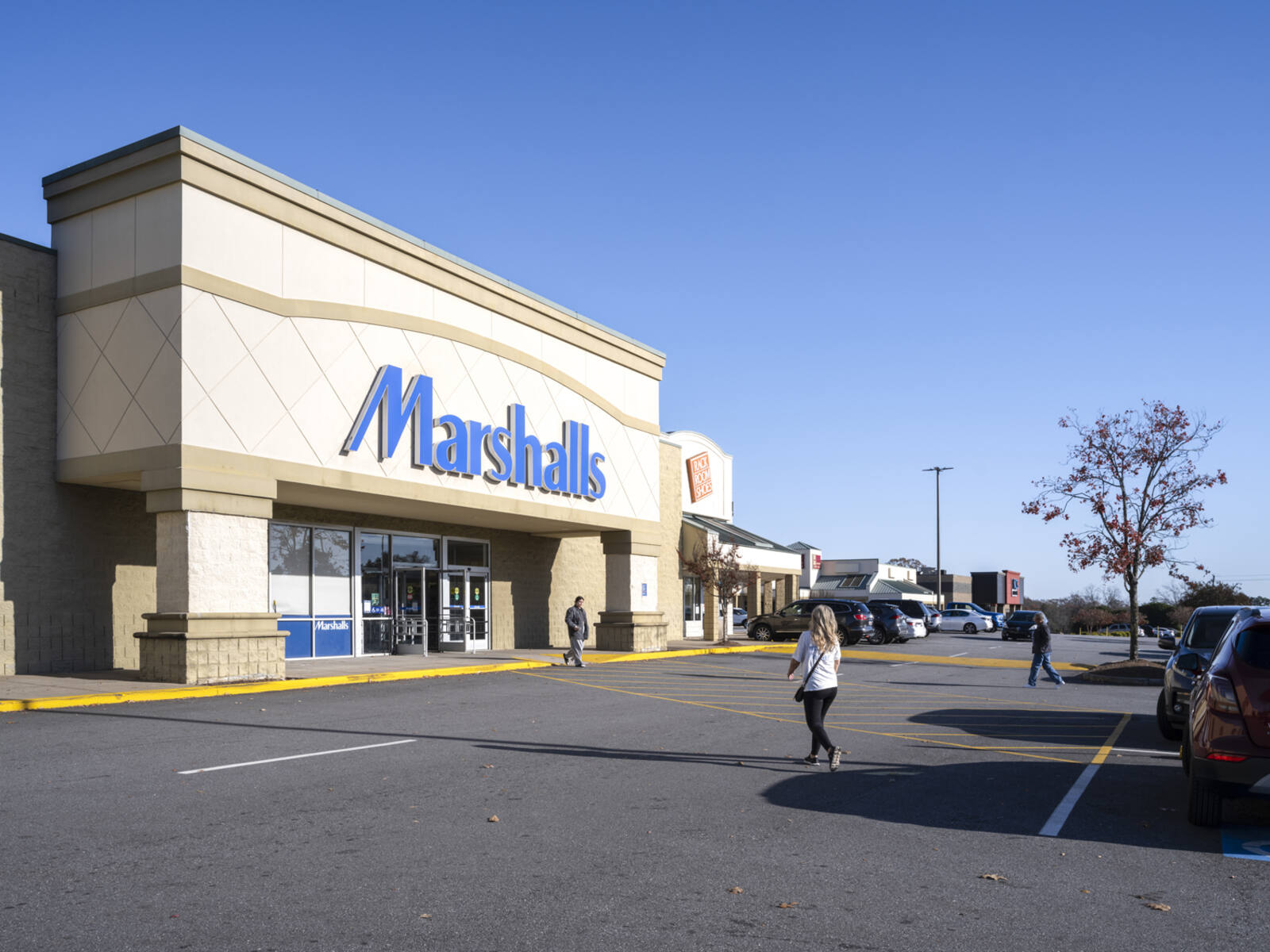 Pedestrians cross access road to Marshalls in a parking lot.