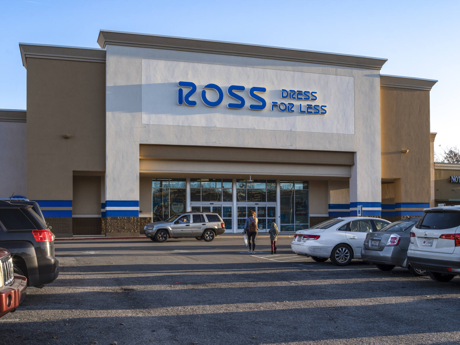 Woman and child approach Ross Dress for Less store down row in a parking lot.