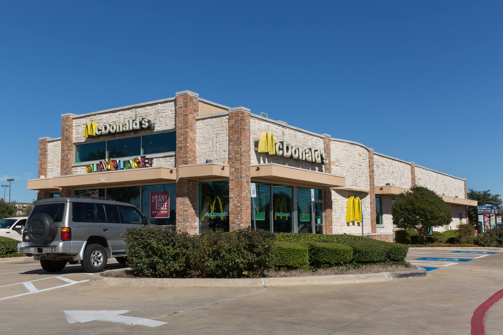 Grey jeep parked at McDonald's with small trees and shrubs.