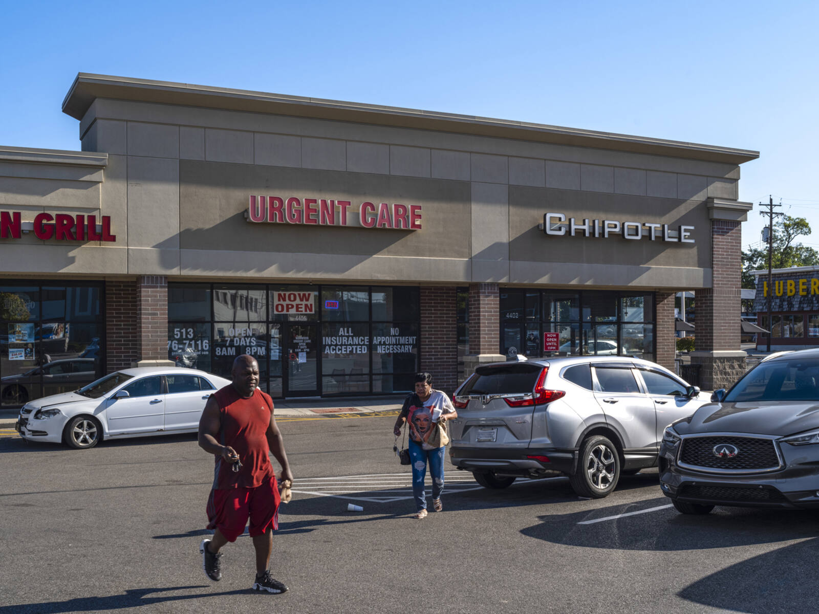 Man and woman walking in parking lot of Chipotle and Urgent Care.