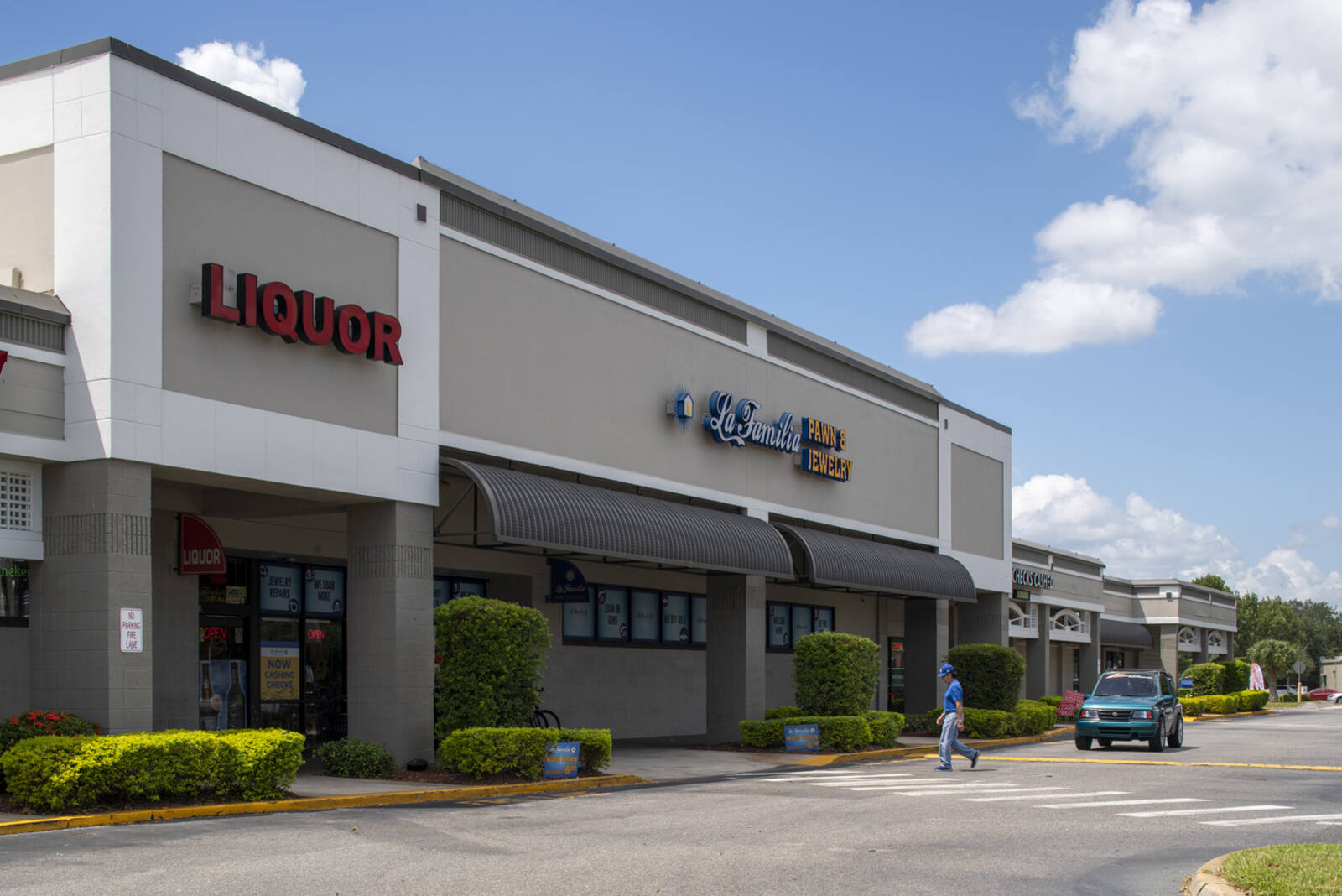 Person walking into hedge lined entrance of La Familia Pawn & Jewelry