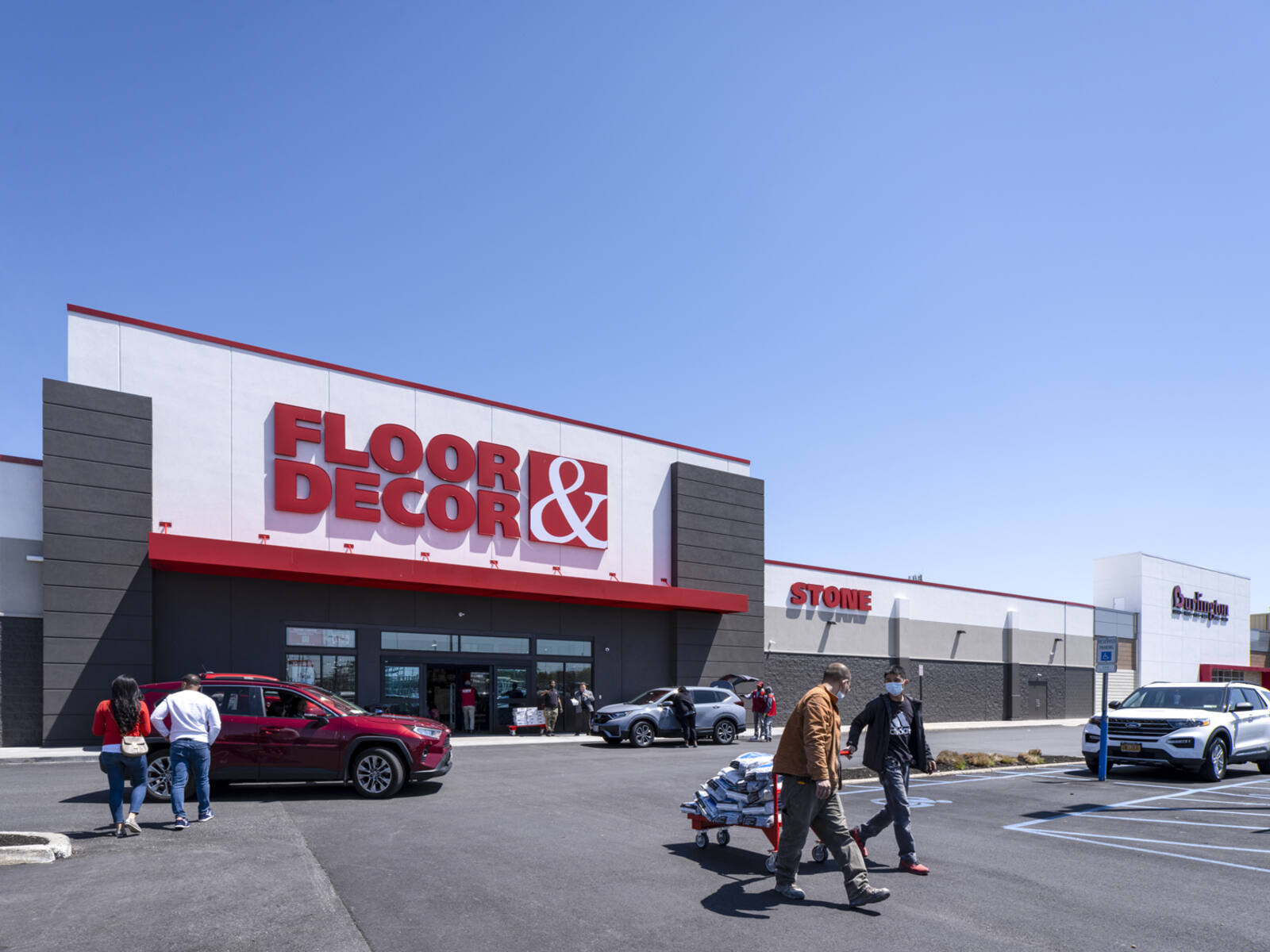 Two men with purchased supplies on a cart leaving Floor & Decor.