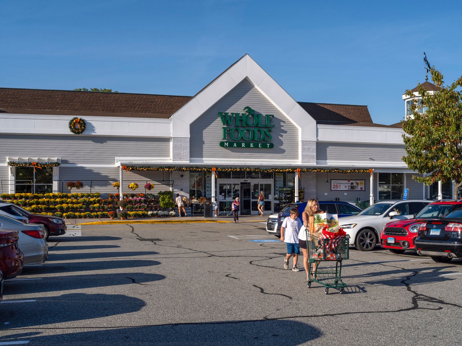 Family with shopping cart exit Whole Foods Market into parking lot.