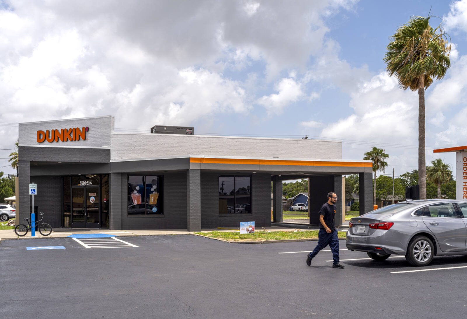 Man in parking lot at Dunkin' with palm trees surrounding.