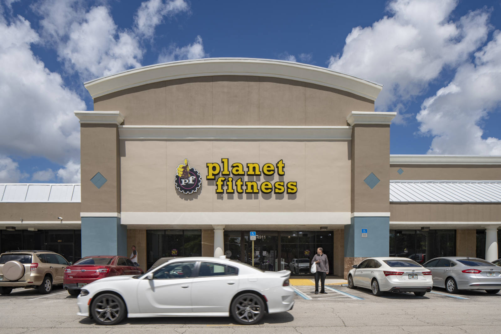 White sports car and shopper in front of Planet Fitness gym in Coconut Creek, FL.