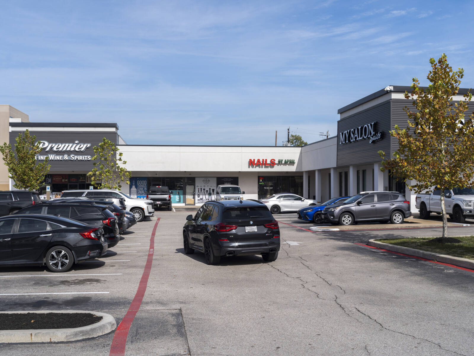 Black SUV on access road in shopping center approaching Premier Fine Wine & Spirits.