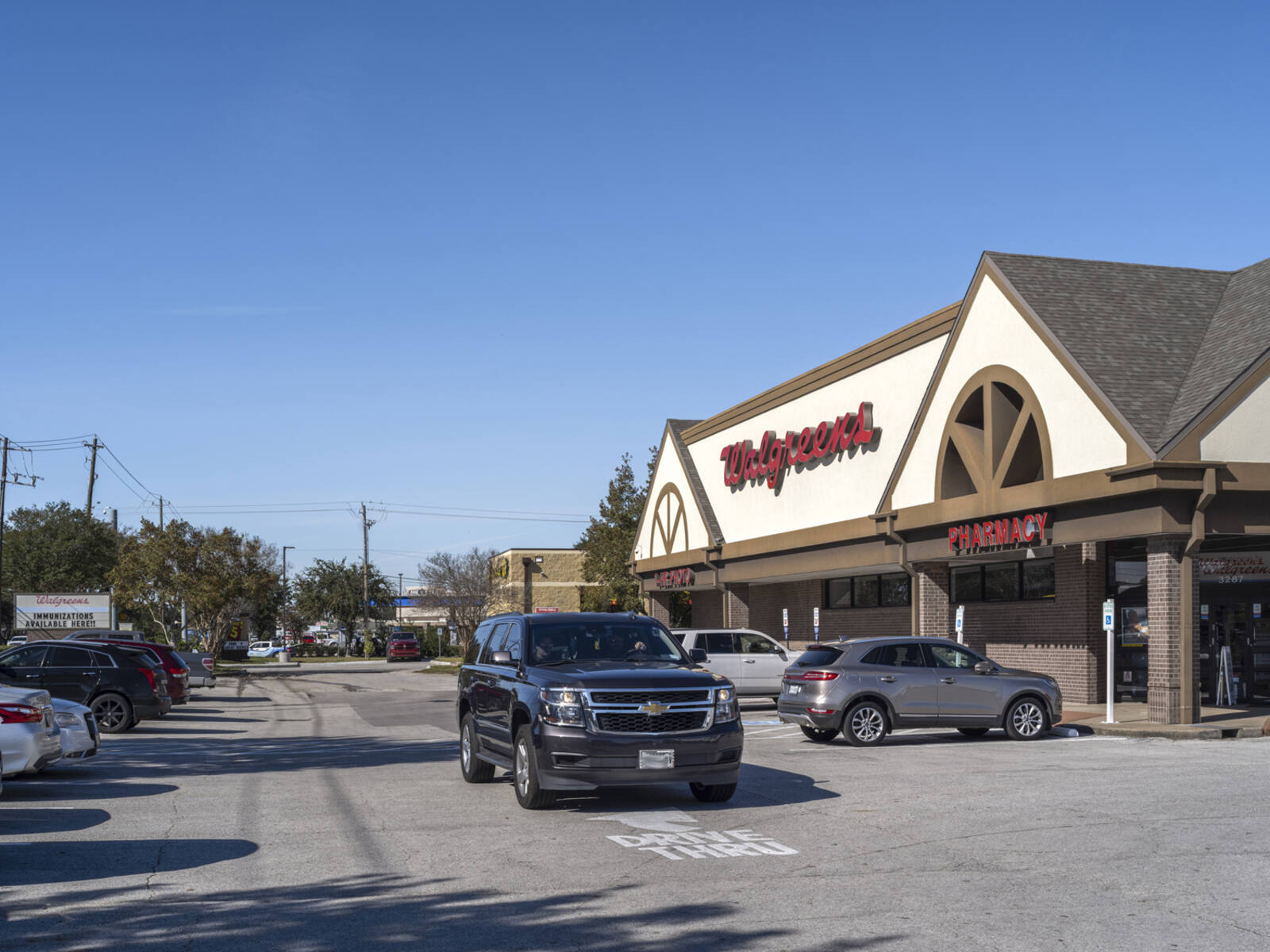 Black SUV driving past Walgreens parking lot and entrance.