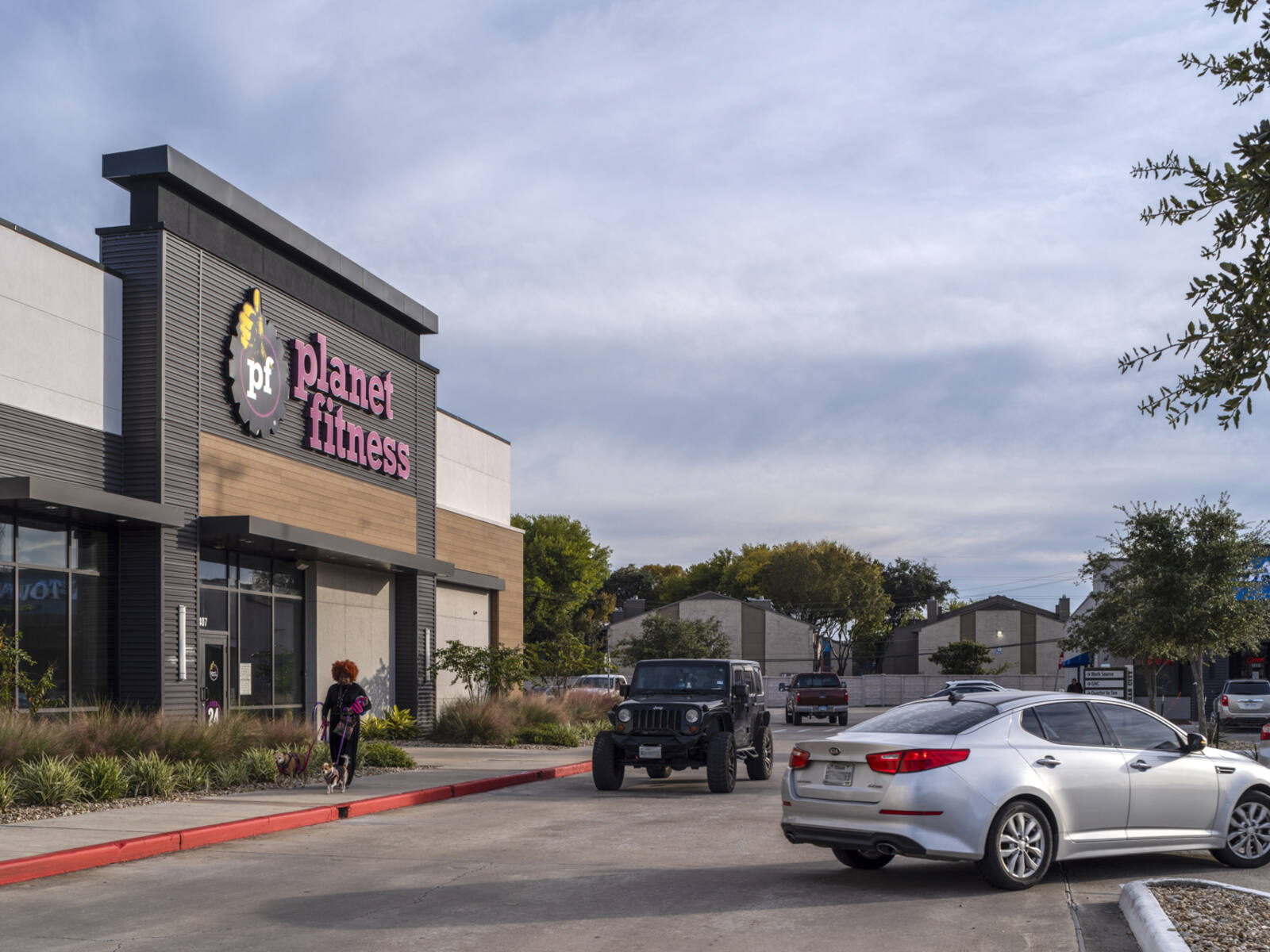 Planet Fitness with busy road in front and pedestrian walking dog on sidewalk.