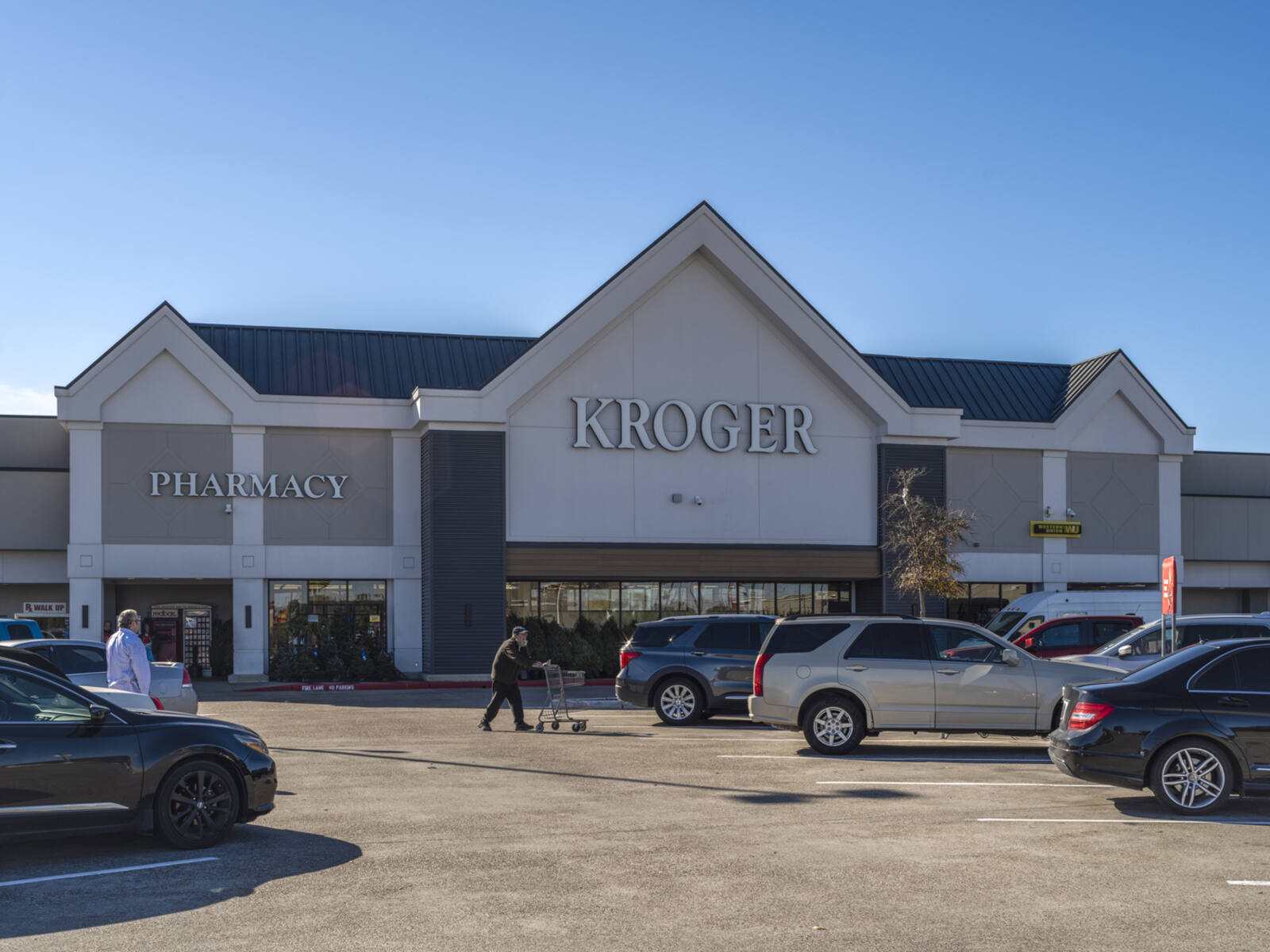 Kroger with customers pushing cars and SUVs in parking lot store entrance.