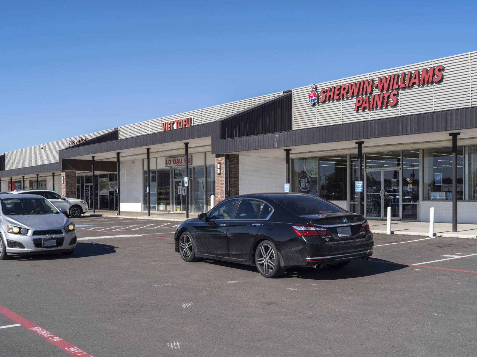 Two cars passing Sherwin Williams Paints on access road at shopping center.