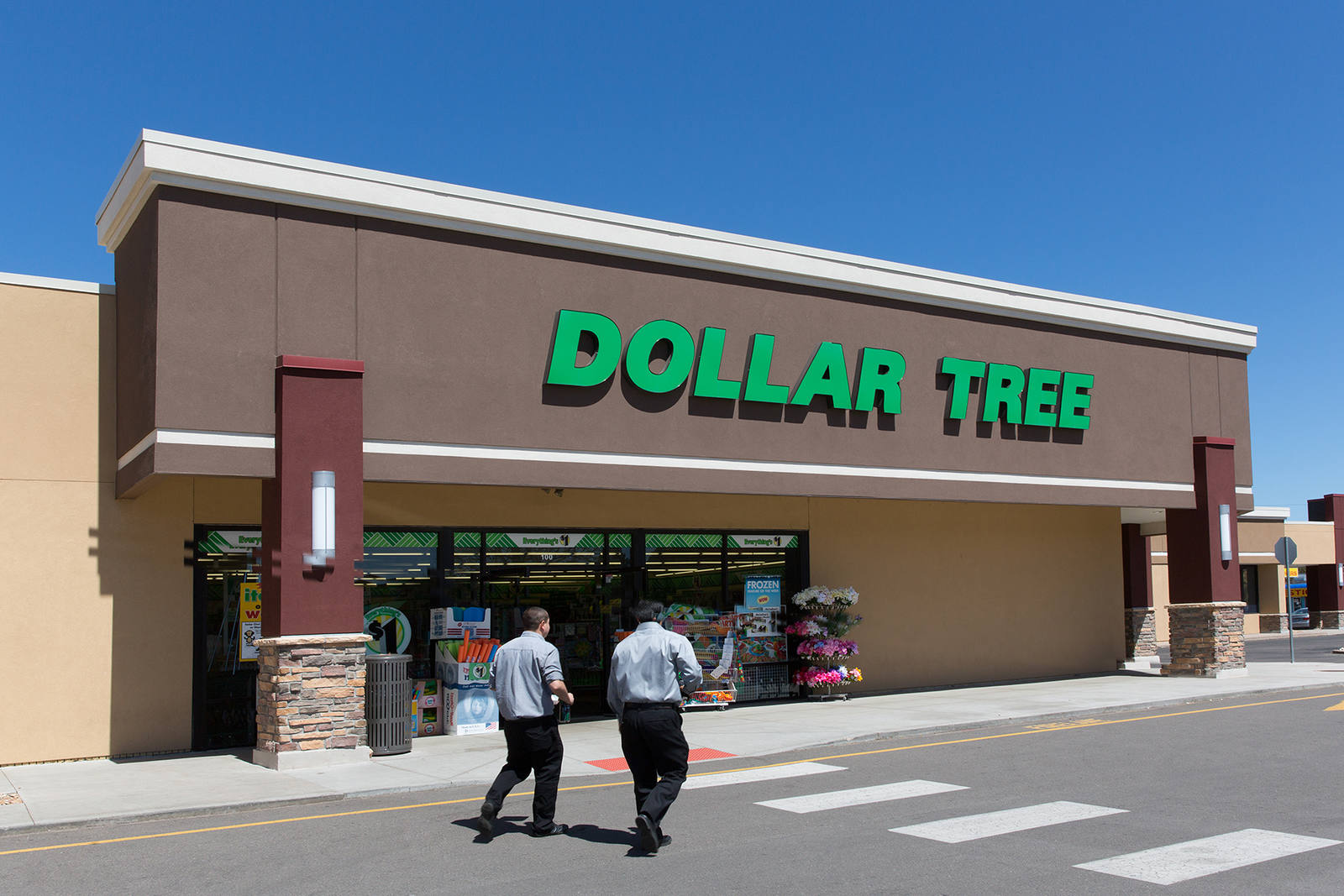 Two people in black pants walking towards the entrance of Dollar Tree on a clear day