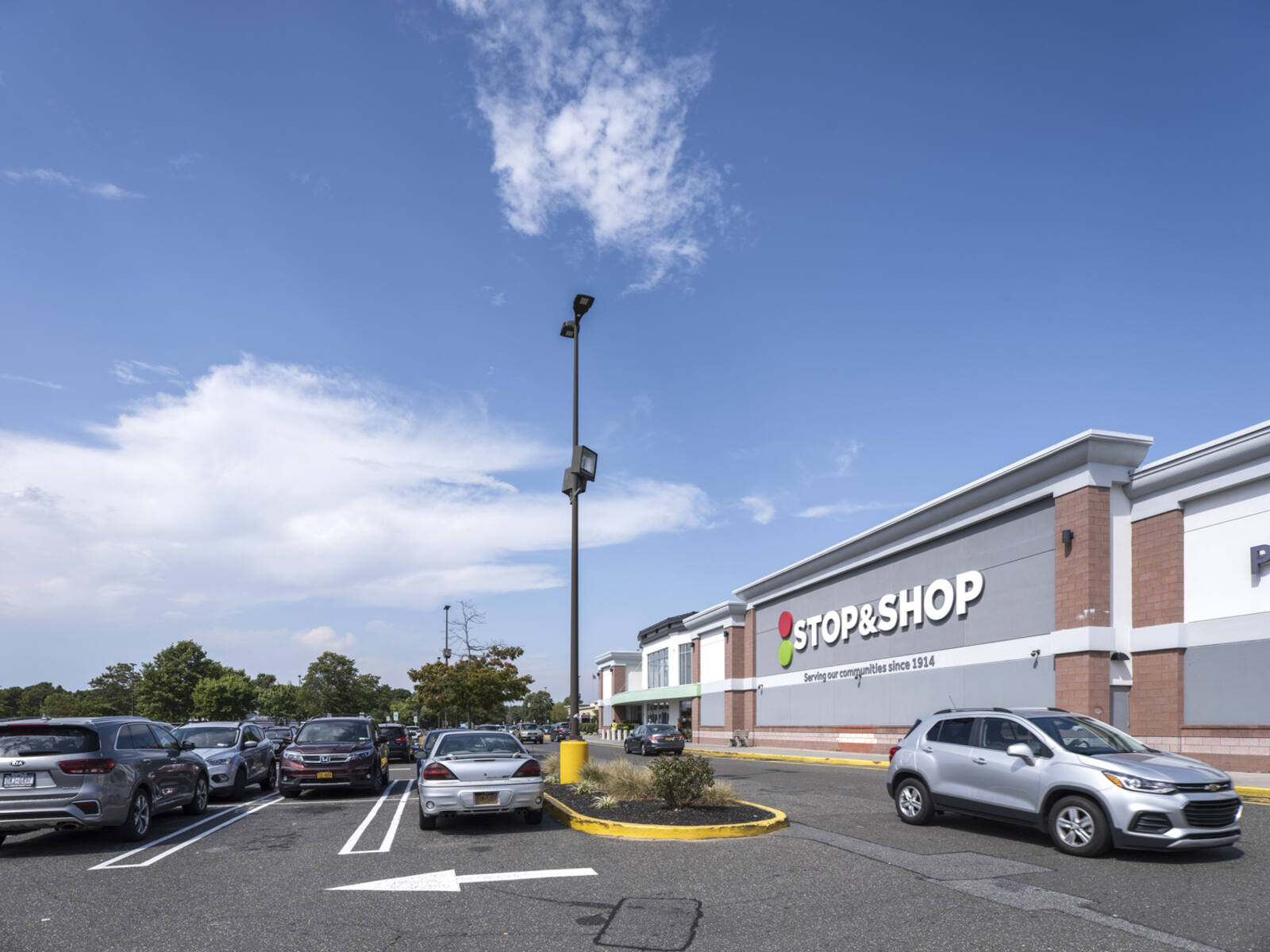 Grey SUV passing Stop & Shop grocery store and busy parking lot.