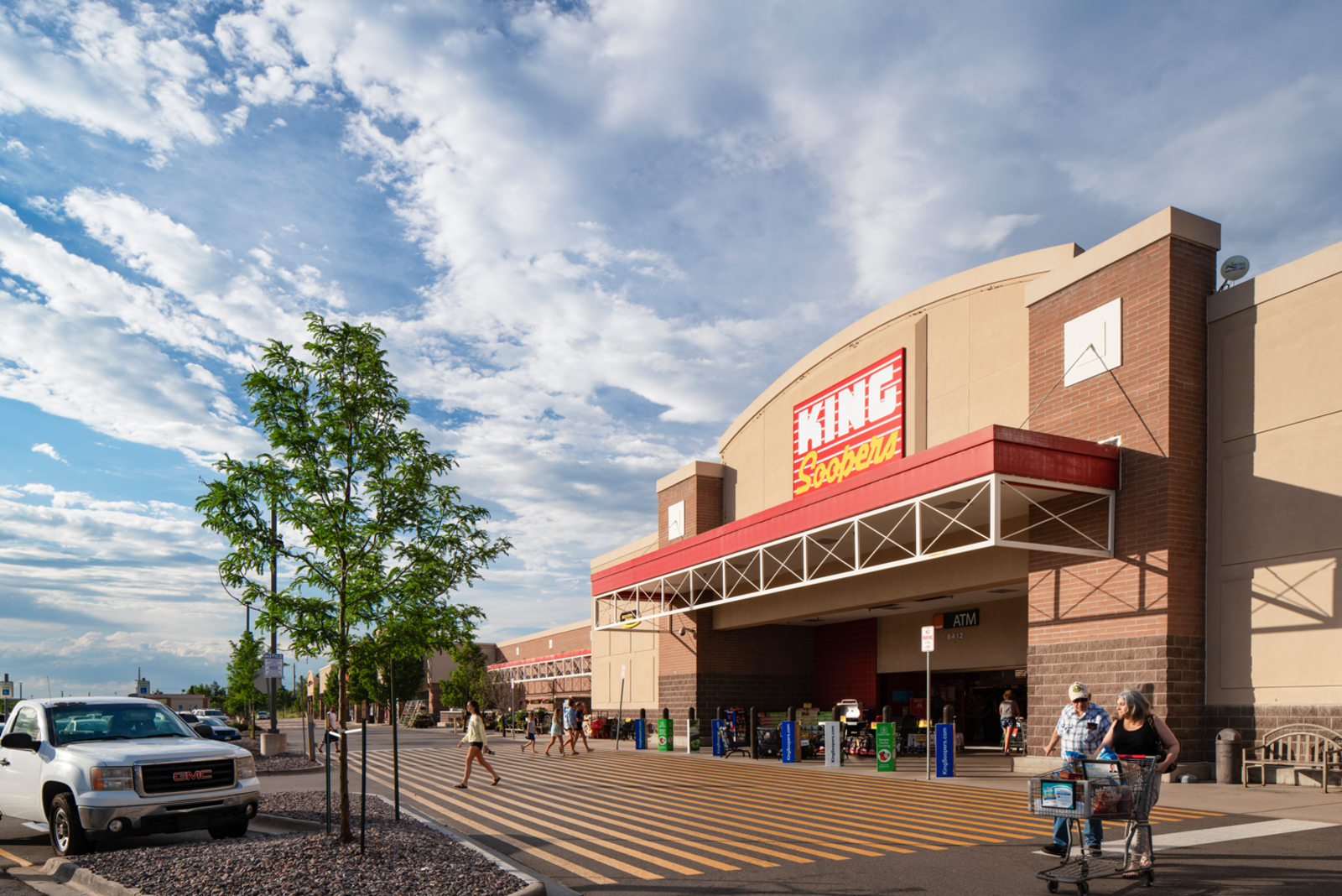 Shoppers enter and exit King Soopers supermarket with a cloudy blue sky in Aurora, CO.