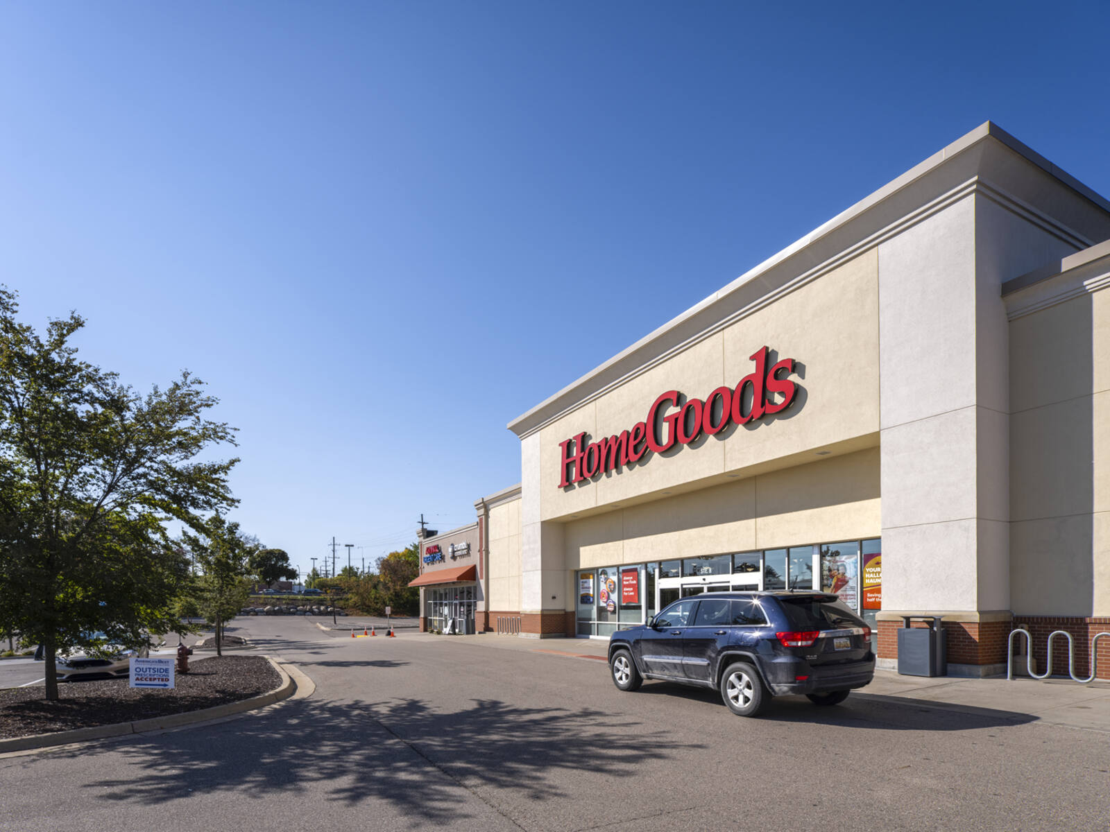 SUV passing HomeGoods with trees and clear blue sky in the background.